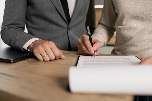 person signing document next to man in suit